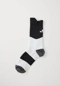 Calzino sportivo in bianco e nero con un design a coste, modelli di presa testurizzati e un tallone imbottito. La zona delle dita è rinforzata con accenti grigi.