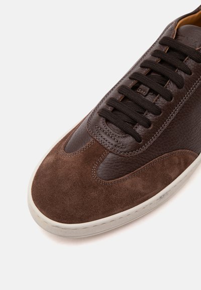 Baskets marron avec bout en daim, côtés en cuir texturé, lacets noirs et semelle blanche sur un fond blanc uni.