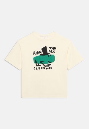 T-shirt crème à manches courtes avec un animal de dessin animé vert portant un chapeau haut-de-forme noir et le texte "The Animals Observatory."