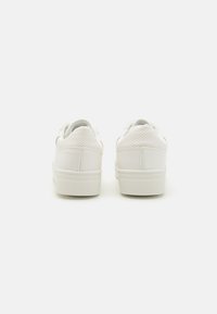 Baskets blanches avec une tige en cuir lisse, des accents perforés au niveau du talon et une semelle extérieure en caoutchouc texturé. Design minimaliste.