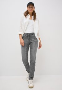 Jeans grigi slim-fit con una texture sbiadita, cinque tasche e vita leggermente alta. Abbinati a un top bianco senza maniche e una camicia bianca con bottoni.