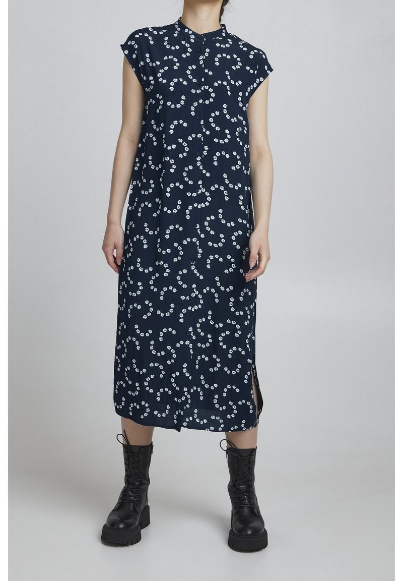 Robe sans manches bleu marine avec motif floral blanc, boutonnée à l'avant, fentes latérales et coupe droite, associée à des bottes de combat noires à lacets.