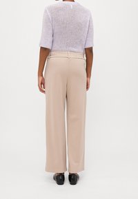 Pletený svetr levandulové barvy s krátkým rukávem, spárovaný s béžovými širokými kalhotami. Kalhoty mají strukturovaný pas a hladkou látku.