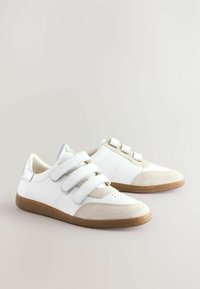 Biała sneakersy z trzema rzepami, zamszowymi akcentami i teksturowaną gumową podeszwą. Posiadają górę ze gładkiej skóry i perforowany czubek.