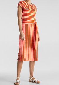 Czerwona i biała sukienka w paski z krótkimi rękawami, do kolan, z przewiązywaniem w talii, z bocznymi rozcięciami, wykonana z miękkiego, lekkiego materiału.