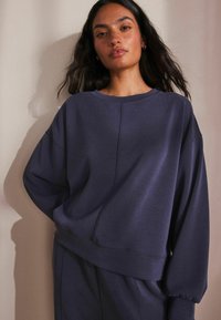 Donkerblauwe sweatshirt met een ontspannen pasvorm, voorzien van lange mouwen, een brede halslijn en zichtbare naden op een gestructureerde stof.