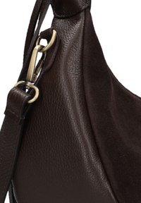 Gros plan sur un sac à main en cuir brun foncé et en suède, avec une sangle ajustable et un fermoir en métal doré.