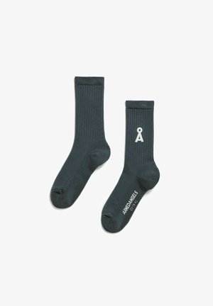 Donkergroene ribbelsokken met een wit logo en merkje op de zool, gemaakt van een zacht, rekbaar materiaal.