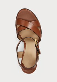Hnedé kožené sandále s prekríženými popruhmi, otvorenou špičkou, členkovým remienkom a zlatými kovovými prvkami. Hladká textura a minimalistický dizajn.