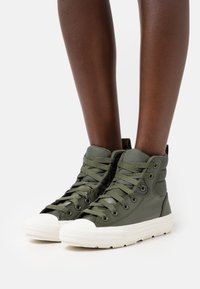 Zapatillas altas verdes con material texturizado, puntera redonda de goma blanca y cordones verdes a juego, con ojales metálicos y cuello acolchado.