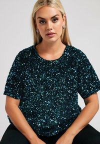 Top corto a maniche corte nero e teal decorato con paillettes, presenta un collo rotondo e una vestibilità rilassata, con una texture liscia e una finitura lucida.