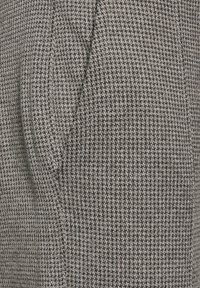 Šedá a černá tkanina s vzorem houndstooth, která má texturovaný povrch a ukazuje klasický tkaný design. Má střední hmotnost, což ji činí vhodnou pro svrchní oděvy.