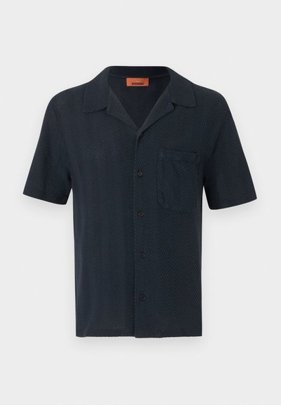 Chemise bleu marine à manches courtes avec boutons, col style camp et poche poitrine, présentant un motif en maille chevrons subtil.