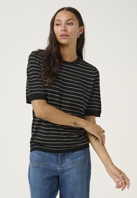 Suéter negro de manga corta con rayas blancas horizontales. Cuello y puños acanalados. Textura suave, corte holgado, combinado con jeans azules.