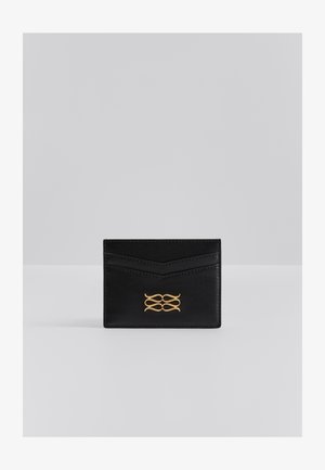 Čierny kožený púzdro na karty s chevron dizajnom, siahajúce zlatým emblémom na prednej strane a tenkým profilom pre jednoduché nosenie.
