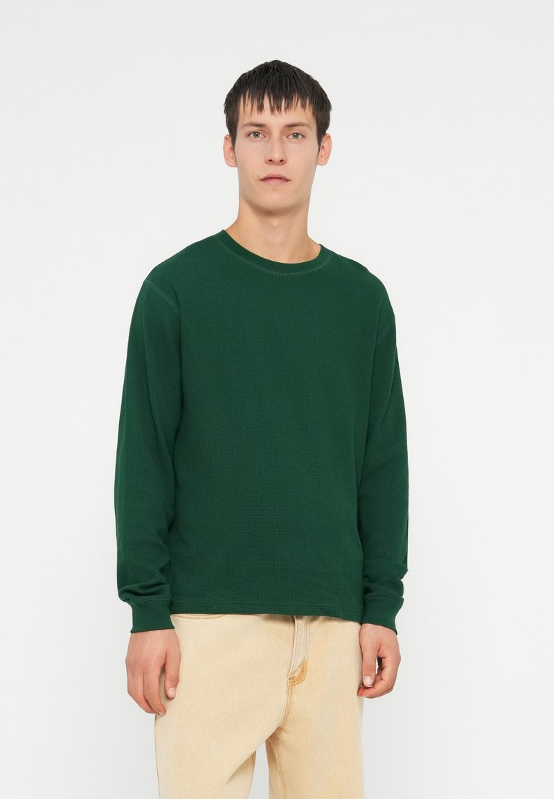 Groen langemouwen shirt met een ronde hals en ribbeltextuur, gecombineerd met lichtgekleurde spijkerbroek.