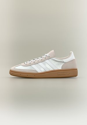 Baskets Adidas blanc et beige clair avec semelle en gomme, bandes blanches et lacets, vues de côté sur fond neutre.