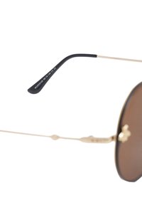 Gafas de sol redondas con lentes marrones, montura de metal dorado y varilla de plástico negro que muestra el número de modelo. Diseño minimalista, ligero.