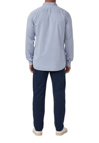 Lichtblauwe longsleeve shirt met knoopmanchetten en een afgeronde zoom, gecombineerd met marineblauwe broek en witte sneakers, gezien vanuit de achterkant.
