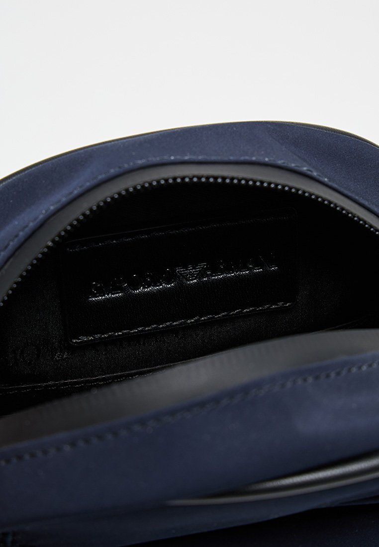 Interior de bolsa de tela azul marino con textura suave, que presenta una etiqueta de cuero negro con marca en relieve y cierre con cremallera.