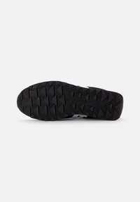 Zwarte sportieve schoen zool met een robuuste textuur en driehoekige profiel voor grip en logo detail.