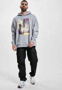 Sudadera gris con diseño gráfico frontal, combinada con pantalones cargo negros con bolsillos laterales y zapatillas blancas con acentos plateados.