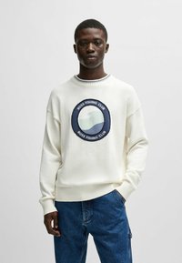 Felpa bianca a maglia con un logo ricamato rotondo "BOSS FISHING CLUB" che presenta onde blu. Polsini e orlo a coste, vestibilità rilassata.