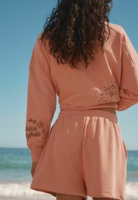 Set di felpa e pantaloni corti in cotone rosa con design ricamati sulle maniche e sul retro, caratterizzato da una vestibilità rilassata e una texture morbida.