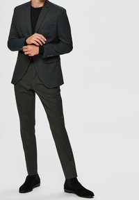 Dark gray blazer and matching tailored trousers in a slim fit, featuring a single chest pocket, paired with black ankle boots.