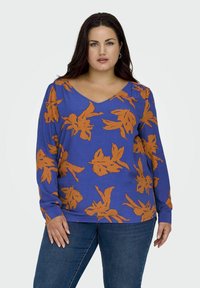 Langarmshirt in leuchtendem Blau mit orangefarbenem Blumenmuster, mit V-Ausschnitt und weichem, strukturiertem Stoff. Kombiniert mit Jeans.