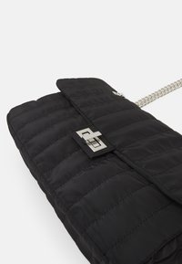 Borsa a spalla nera trapuntata in nylon con accessori in argento lucido, dotata di chiusura a pattina e tracolla a catena. Superficie testurizzata con sezioni in rilievo.