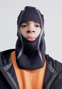 Černá balaclava s prodyšnými síťovinovými panely, navržená pro těsné padnutí a reflexními akcenty, určená pro použití v chladném počasí.