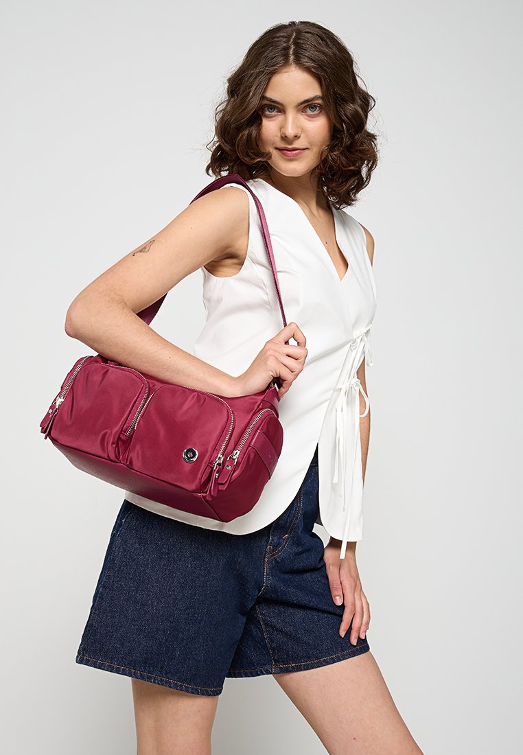 Bordeauxfarbene Handtasche aus glattem Nylon, mit zwei vorderen Reißverschlüssen, einem runden Logo und einem langen Schultergurt.