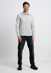 Jasnoszara koszula na guziki z wzorem w kratę, w połączeniu z ciemnymi dżinsami i czarnymi sznurowanymi butami. Tkanina wydaje się gładka i dopasowana.