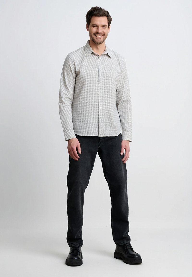 Jasnoszara koszula na guziki z wzorem w kratę, w połączeniu z ciemnymi dżinsami i czarnymi sznurowanymi butami. Tkanina wydaje się gładka i dopasowana.