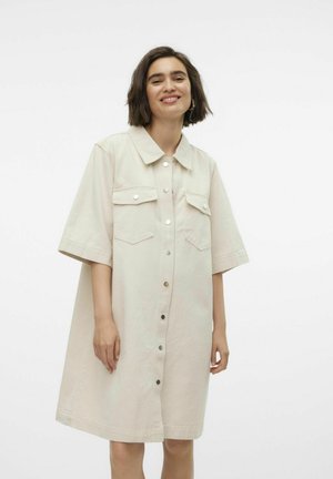 Lichtbeige shirtjurk van katoen met korte mouwen, knoopsluiting aan de voorkant en twee borstzakken, met een ontspannen silhouet en zachte textuur.