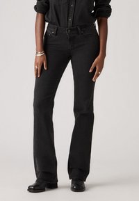 Sorte denim flarejeans med høj talje, der har forlommer og knaplukning. Stoffet har en glat tekstur og minimal syning.