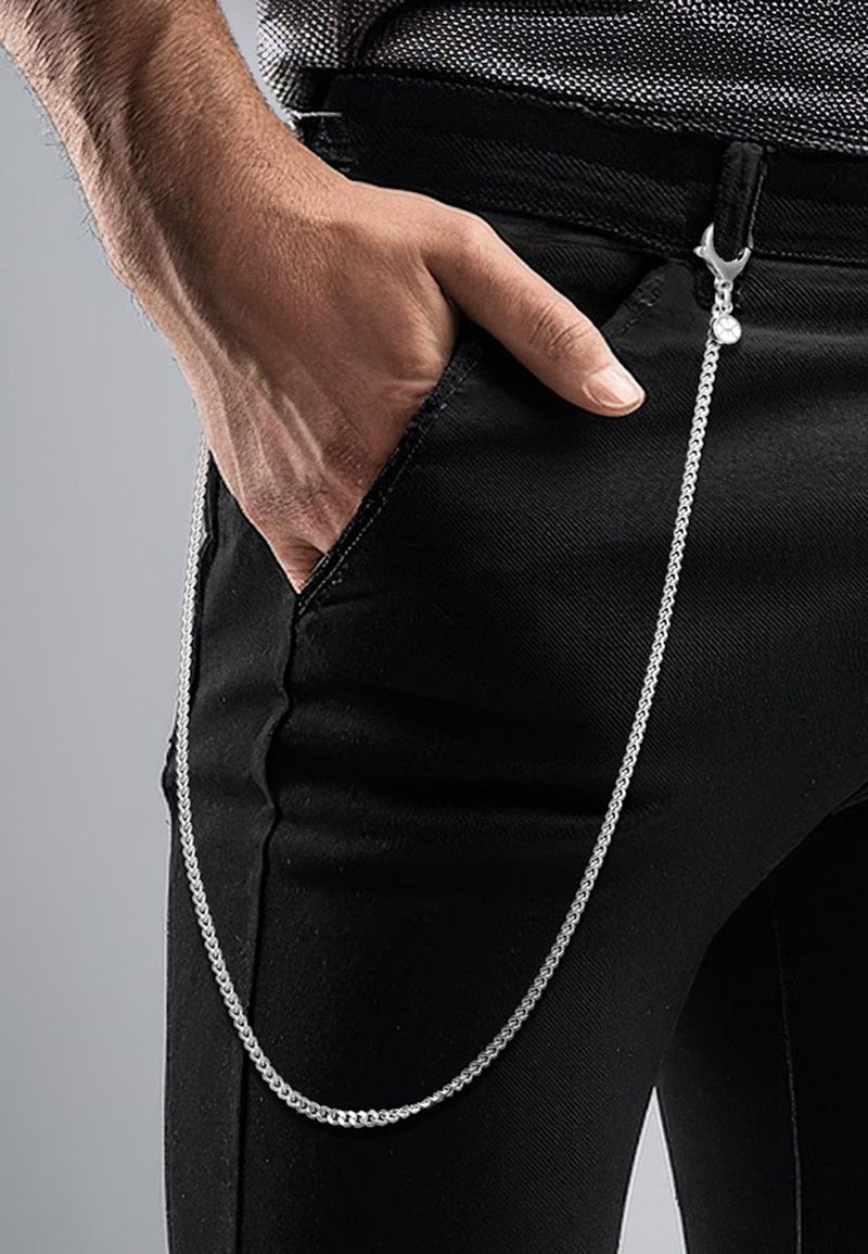 Silverkedja med en spänne som hänger från en ficka på svarta byxor, vilket framhäver en slank, metallisk textur.
