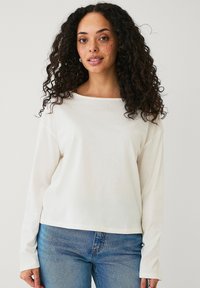 Witte langlopende T-shirt met een bootnek, zachte stof en een relaxte pasvorm, gecombineerd met blauwe spijkerbroeken.