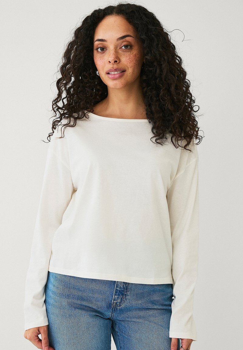Witte langlopende T-shirt met een bootnek, zachte stof en een relaxte pasvorm, gecombineerd met blauwe spijkerbroeken.