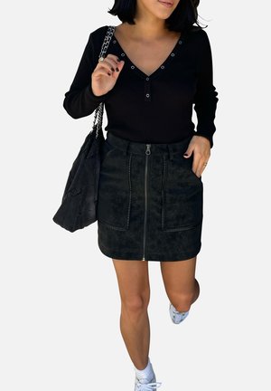 Top noir à manches longues à côtes avec décolleté en V et détails de boutons, associé à une mini-jupe en daim noir zippée avec poches avant et coutures visibles.