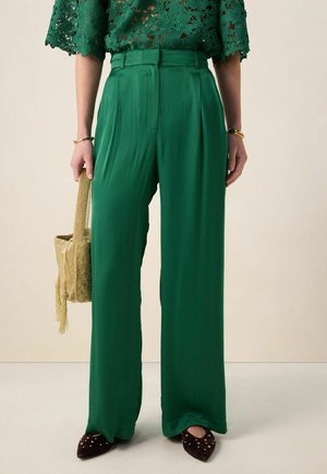 Groene, wijde broek met wijde pijpen van gladde stof met plooien. Heeft een hoge taille en zijzakken, gecombineerd met een gestructureerde gouden handtas.