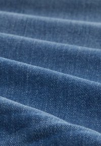 Tejido de denim en azul profundo, con una textura de tejido visible y sutiles variaciones de color, doblado en múltiples pliegues.