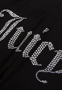 Tissu noir orné de strass argentés décoratifs disposés en motifs courbes et ornés, ressemblant à des lettres ou symboles stylisés.
