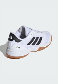 Baskets de sport blanches avec des accents noirs et trois bandes. Présente une tige en mesh, une semelle rembourrée et une semelle extérieure en caoutchouc. Texte "LIGRA" sur le talon.