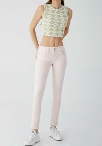 Oříznutý top bez rukávů se zelenobílým diamantovým vzorem, doplněný těsně padnoucími světle růžovými džíny a bílými teniskami. Hladká látka, střih na tělo.