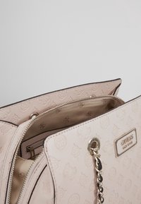 Rosa handväska med präglat logomönster, dragkedja och beslag i silverton. Insidan har beige foder och organiseringsfickor.