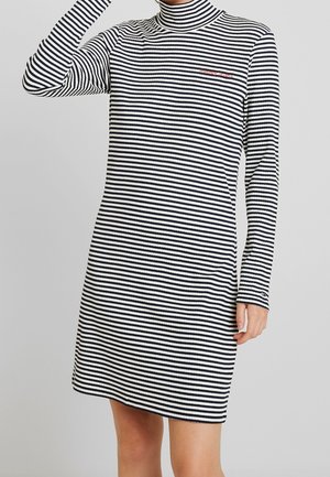 Schwarz-weiß gestreiftes, langärmliges Rollkragenkleid, das von einer Person getragen wird und bis zur Mitte des Oberschenkels reicht, mit einem erhobenen Arm.