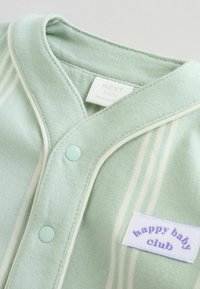 Tenue de bébé vert clair avec des rayures blanches, présentant une texture douce, des fermetures à pression et une étiquette « happy baby club » en violet sur un patch blanc.