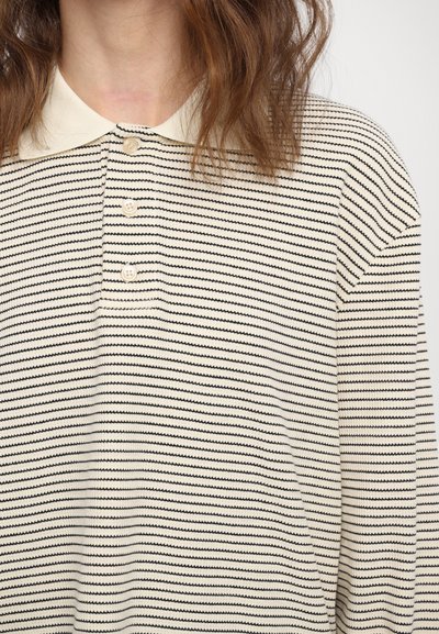 Polo shirt a righe in maglia con righe orizzontali alternate nere e crema, colletto crema e placket con tre bottoni. Texture morbida.